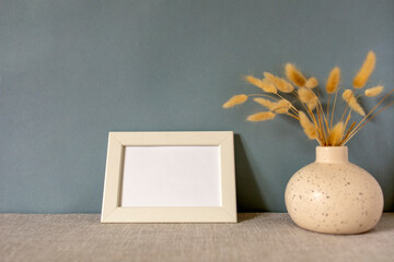 The layout of an empty photo frame on the table. A vase with dry grass. A minimalistic workspace. A place to copy.