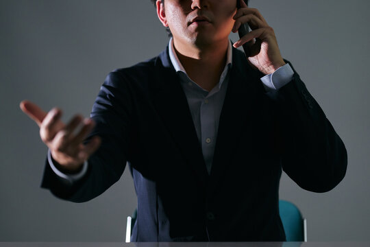 暗い室内でスマートフォンで通話中に相手と口論になる怒るスーツを着た悪徳業者
