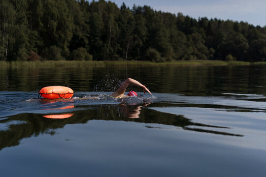 Swimmer in a lake with a safety buoy, wearing a red cap and goggles