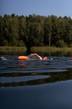 Swimmer in a lake with a safety buoy, wearing a red cap and goggles