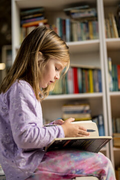 Little girl reading book in the library or book shop