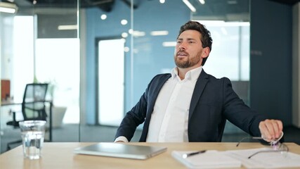 Satisfied professional businessman in a dark suit and white shirt at an office desk closes laptop, removes glasses, and leans back, feeling happy and content in a modern office. - Powered by Adobe