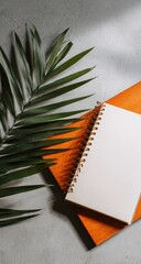 Blank notebook, orange cover, palm leaf, gray background