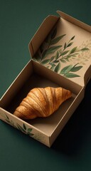 A croissant nestled in a kraft paper box with botanical design