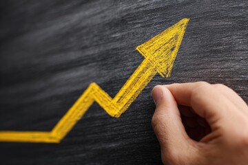Hand draws a yellow upward trend line graph on a dark chalkboard