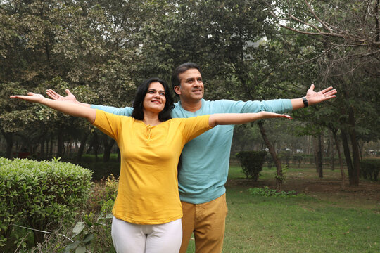 Happy Indian couple spreading hands relaxing at garden outdoor. Romantic and Attractive couple in love, fun, hugging outside, spending leisure time together, relationship and people concept.