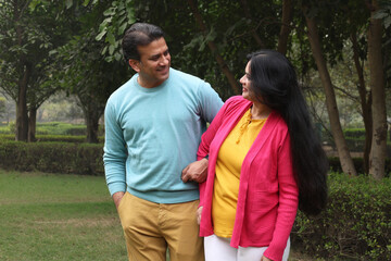 Obraz premium Indian happy young couple standing and looking each other with love and care. Indian Smiling young couple holding hands and standing outdoors at the nature. Celebrate the form of love at park