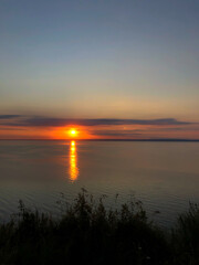Sun and large river Volga, Russia. The sun is setting over the water. The water is calm and still. The sky is a mix of orange and purple