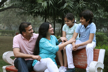 Happy Indian family spending leisure time at the nature outdoor park. Happy indian couple with kids embracing by looking at camera at garden. Concept of relationship, togetherness and family lifestyle