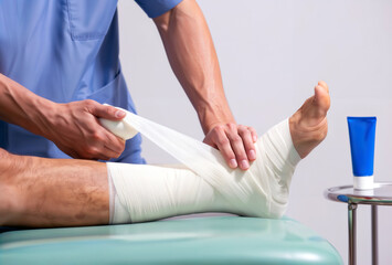 A medical professional wraps an injured ankle with a compression bandage in a clinic.