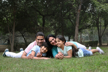 Fototapeta premium Happy Indian family spending leisure time at the nature outdoor park. Happy indian couple with kids embracing by looking at camera at garden. Concept of relationship, togetherness and family lifestyle