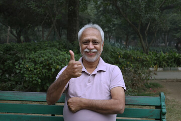 Indian  happy senior man showing thumbs up feels freedom, fun and spending time at the park after retirement