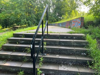 Empty paved pathway with graffiti wall and green trees on a sunny day. Urban landscape with nature contrast, concept of freedom, street art, and modern outdoor lifestyle.