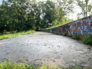 Empty paved pathway with graffiti wall and green trees on a sunny day. Urban landscape with nature contrast, concept of freedom, street art, and modern outdoor lifestyle.