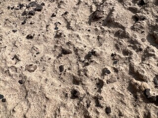 Dry sandy ground with scattered rocks and footprints. Natural texture background useful for design, construction, environment, geology, and outdoor nature concepts.