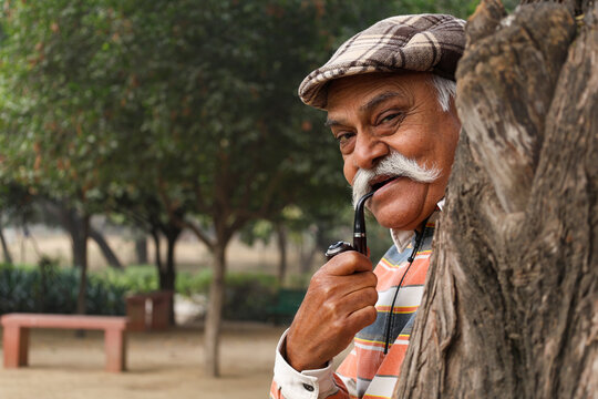 Portrait of a Indian happy senior man standing with holding cheroot pipe at outdoor park. Indian old man freedom and travel after retirement and happiness senior citizen lifestyle