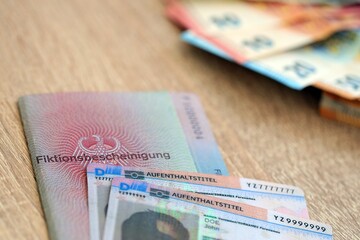 German Permanent resident card and document specimen with euro money bills lies on wooden table
