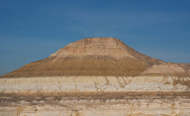 Majestic sandstone mesa in Bozzhira canyon, Mangystau, Kazakhstan, surrounded by layered white and yellow cliffs under a clear blue sky, showcasing unique geological formations.