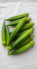 Obraz premium A cluster of fresh, green okra pods arranged on a textured white cloth, showcasing their ribbed texture and vibrant color.