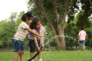 Indian happy and cute kid girls playing and splashing water pipe in garden. Background of green...