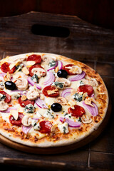 Pizza with chorizo ​​sausage, mozzarella cheese, and black olives. Rustic wooden background. Soft focus.	