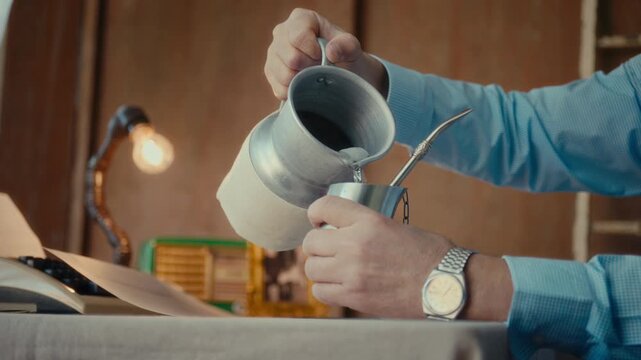 Man pouring hot water into a traditional mate cup with a metal thermos on the table. Terer&eacute;, a Latin American tradition, is a concept.