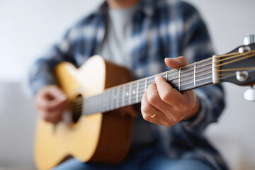 Fototapeta premium Acoustic guitar player strumming wooden instrument with fingers, wearing casual plaid shirt, creating warm and relaxed music atmosphere