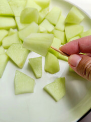 Hand Holding a Sweet Honeydew Melon Wedge on a Wooden Skewer for Easy Snacking