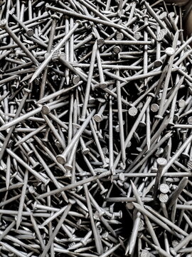Pile of shiny new nails scattered randomly, creating a textured industrial pattern with a metallic sheen, showcasing strength and construction, in a closeup shot.