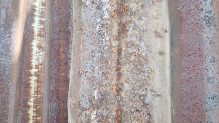 Corrugated metal sheet shows signs of rust and wear in an outdoor setting, revealing textures and patterns of decay, creating a weathered and industrial aesthetic.