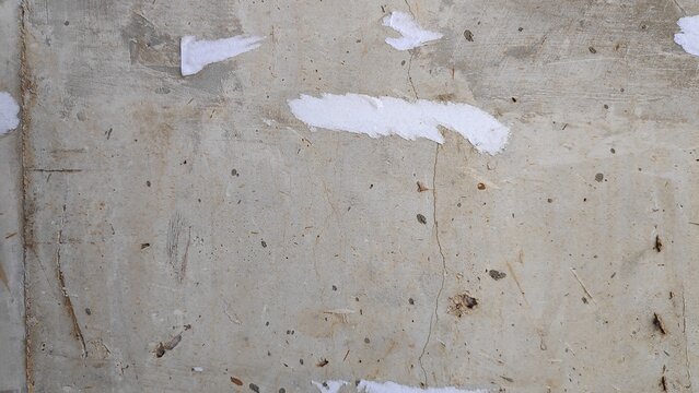 Weathered concrete wall reveals layers of peeling paint and embedded dirt, creating a textured surface with a distressed and aged appearance.