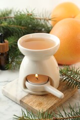 Aroma lamp with burning candle, grapefruits and fir tree branches on white table, closeup