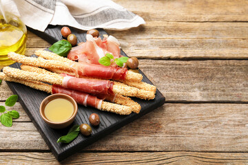 Grissini breadsticks with prosciutto, olives and honey on wooden table. Space for text