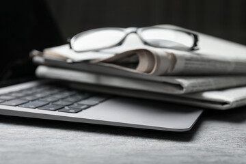 Stack of newspapers, laptop and glasses on grey table, closeup