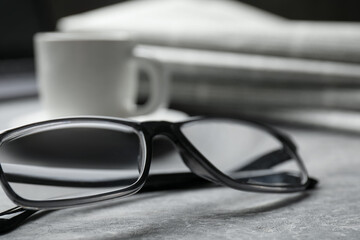Glasses, newspapers and cup on grey table, closeup