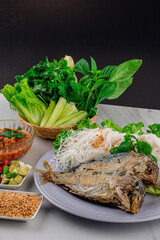 Fried two short bodied mackerel fishes and vegetable on white plate on white table 