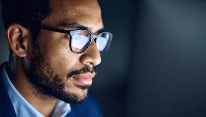 A man wearing glasses concentrating on a monitor in a dark room