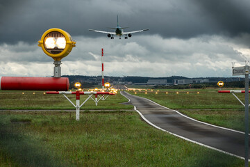 Commercial passenger airplane landing on an illuminated airport runway strip. Ground level, rear of...