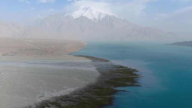 Aerial view of the turquoise waters of Baisha Lake contrasting with the arid land and snow-capped mountains, Baisha Lake, Xinjiang, China.