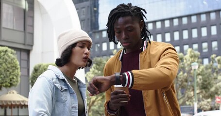 African American couple holding coffee cup checking smartwatch then explaining schedule at plaza - Powered by Adobe