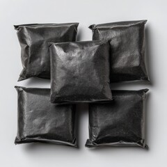 Obraz premium Five sealed black pillow packs are arranged on a plain surface with soft lighting, displaying a minimalist and simple presentation for packaging concepts.