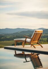 Fototapeta premium A wooden lounge chair sits by a tranquil pool, reflecting the serene landscape of rolling hills and a clear sky in the background.