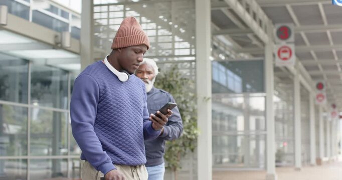 African American friends exchanging phone info at station under canopy after one noticing friend
