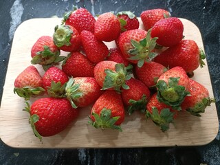 Strawberries on a wooden board on a black stone background.
