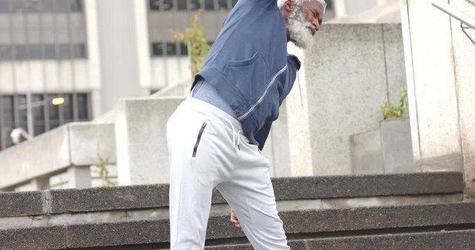 Placing feet African American man in sportswear doing side-bend stretches at plaza steps to warm up