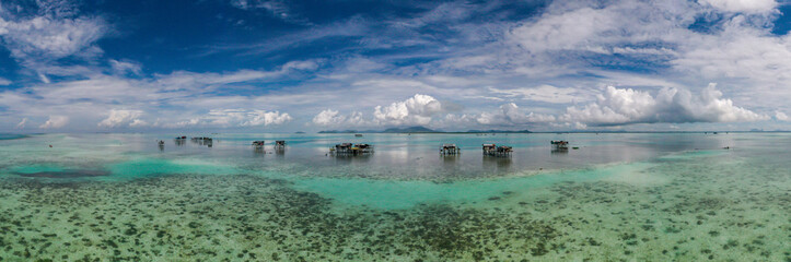 Aerial view of sea gypsy village over clear turquoise waters in Awan Biru Island Semporna, Sabah, Malaysia. Scenic seascape with coral reefs, coastal village, and blue tropical sky.