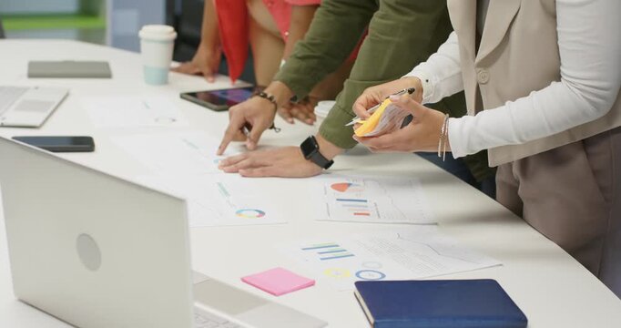 During kickoff, Diverse coworkers pointing at charts, writing notes, analyzing data at office table