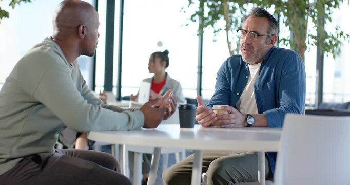 Diverse male colleagues starting discussion leaning forward exchanging ideas over coffee at cafe