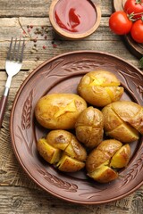 Tasty baked potatoes, fork, spices and tomatoes on wooden table, flat lay