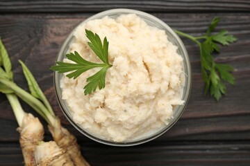 Tasty horseradish sauce with parsley and roots on black wooden table, flat lay